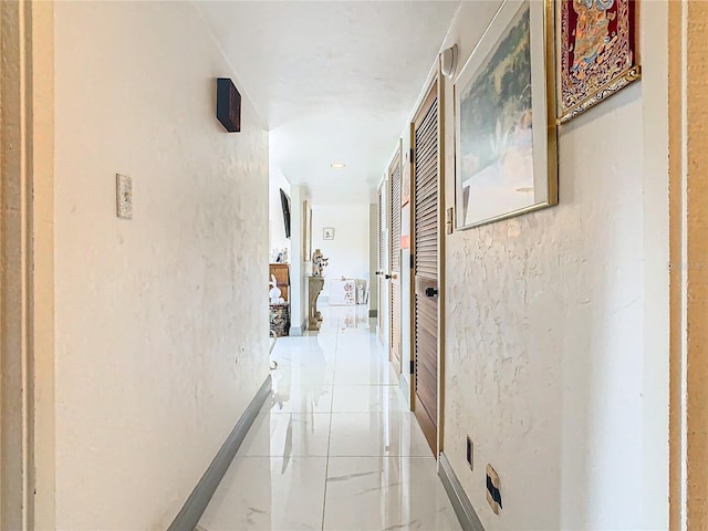 corridor with marble finish floor, baseboards, and a textured wall