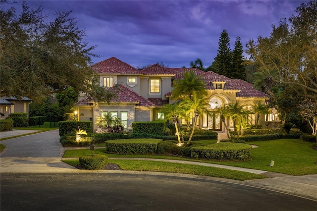 mediterranean / spanish house featuring a lawn, a tile roof, decorative driveway, and stucco siding