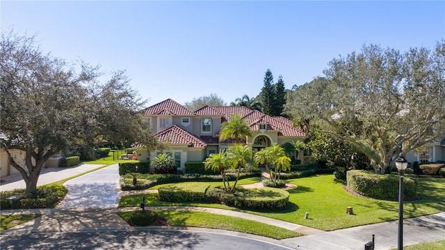 mediterranean / spanish home with stucco siding, a front yard, driveway, and a tile roof