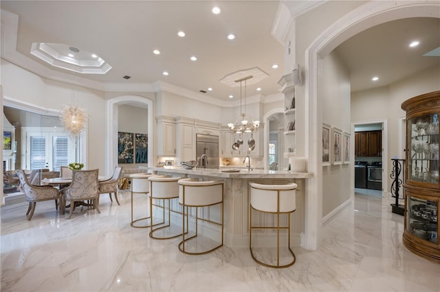 kitchen featuring a chandelier, washing machine and dryer, stainless steel built in fridge, a kitchen breakfast bar, and a high ceiling