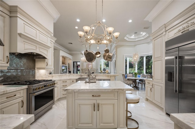 kitchen with premium appliances, marble finish floor, cream cabinets, and ornamental molding