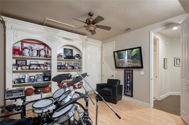 exercise room with a ceiling fan, baseboards, wood finished floors, visible vents, and a textured ceiling