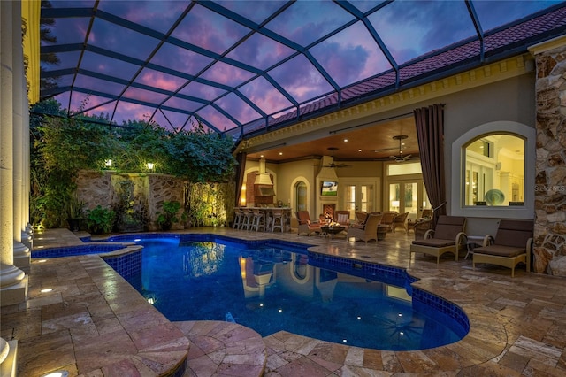 pool at dusk featuring a pool with connected hot tub, outdoor dry bar, a ceiling fan, and a patio area