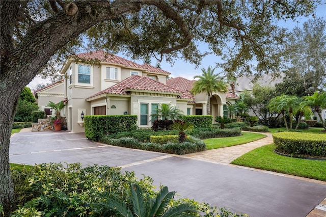 mediterranean / spanish house with stucco siding, driveway, a tile roof, and a garage