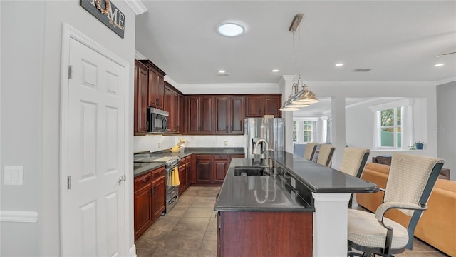 kitchen featuring a center island with sink, dark countertops, hanging light fixtures, appliances with stainless steel finishes, and a sink