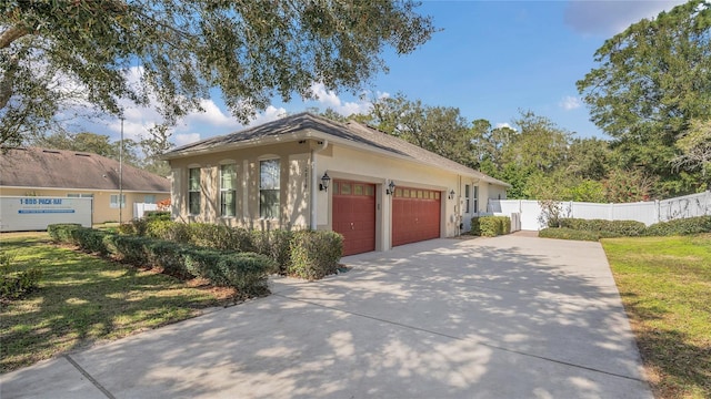 view of front of house with concrete driveway, an attached garage, fence, a front lawn, and stucco siding