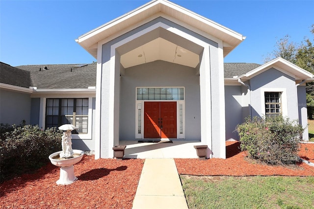 doorway to property featuring covered porch, roof with shingles, and stucco siding