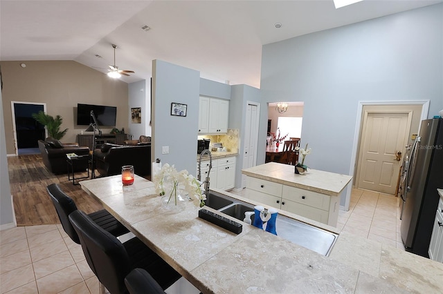 kitchen with light tile patterned floors, white cabinets, open floor plan, a center island, and high vaulted ceiling