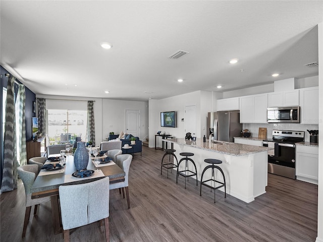 kitchen with a center island with sink, appliances with stainless steel finishes, open floor plan, a breakfast bar area, and white cabinetry