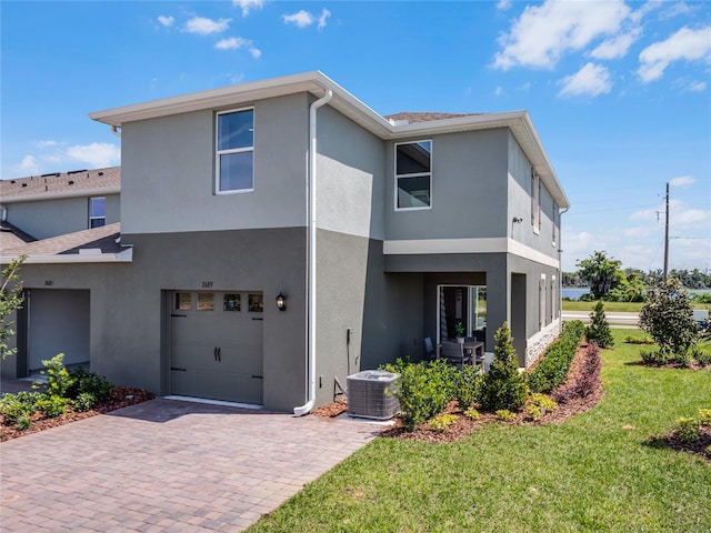 view of front facade featuring a garage, stucco siding, decorative driveway, central air condition unit, and a front yard