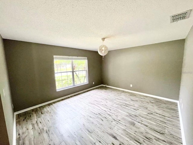 empty room featuring light wood-style floors, visible vents, a textured ceiling, and baseboards