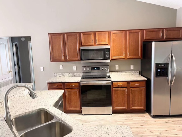 kitchen featuring light wood-type flooring, light stone countertops, stainless steel appliances, and a sink