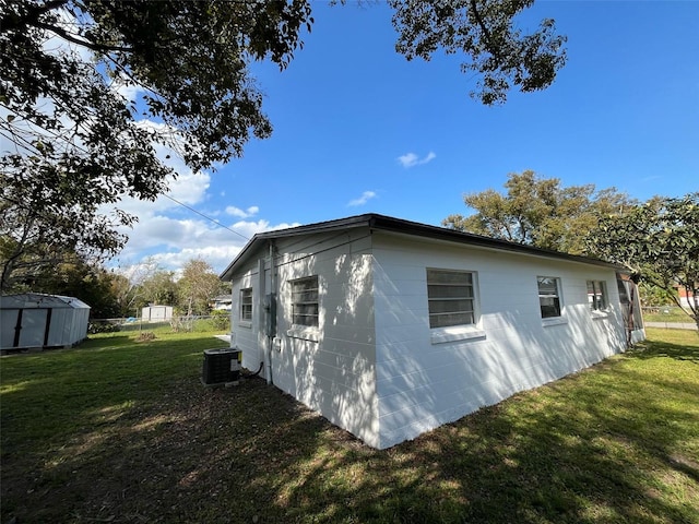 view of side of home featuring concrete block siding, an outbuilding, a storage unit, cooling unit, and a yard