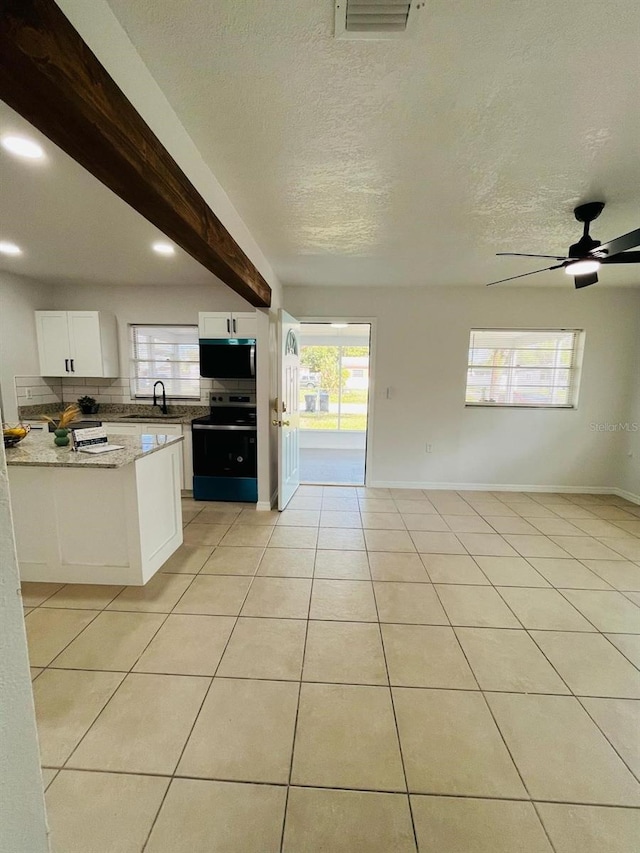 kitchen with beam ceiling, light tile patterned floors, stainless steel microwave, electric range oven, and a sink