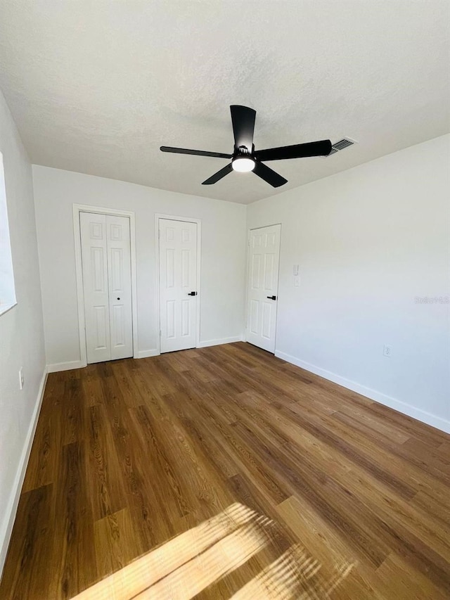 unfurnished bedroom featuring multiple closets, wood finished floors, and baseboards