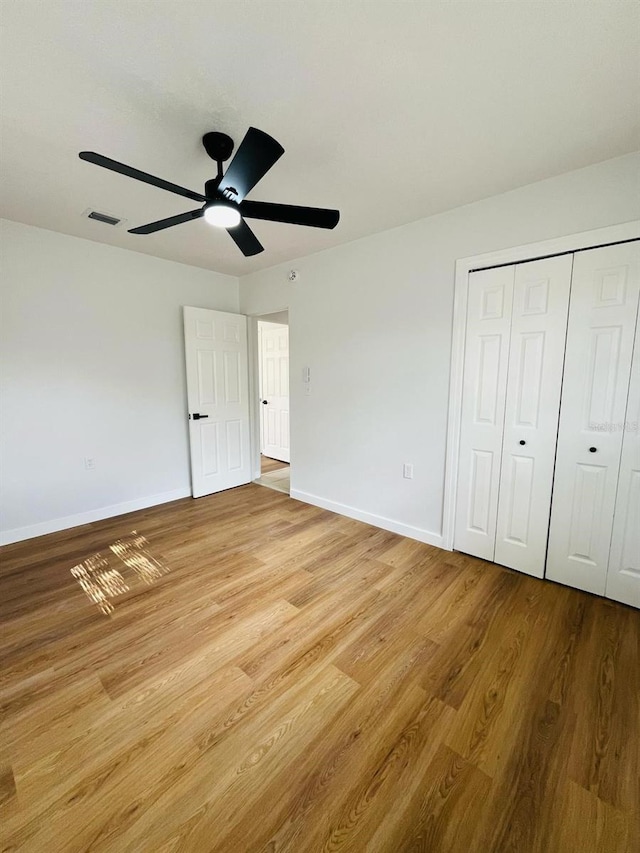 unfurnished bedroom featuring light wood finished floors, a closet, visible vents, a ceiling fan, and baseboards