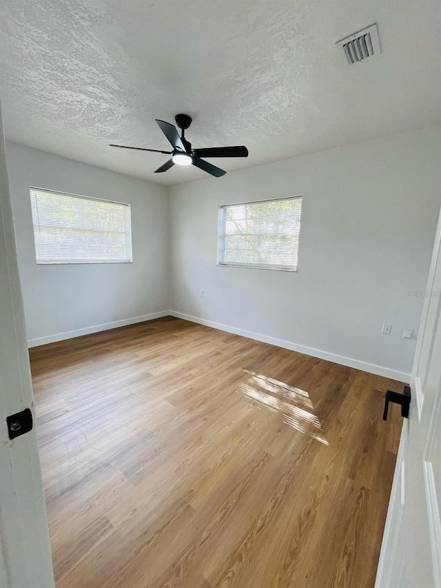 empty room with a textured ceiling, wood finished floors, visible vents, and baseboards