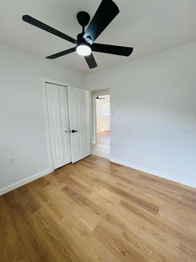 unfurnished bedroom featuring ceiling fan, a closet, light wood-style flooring, and baseboards