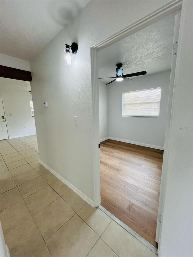 hallway with a textured ceiling, tile patterned flooring, and baseboards