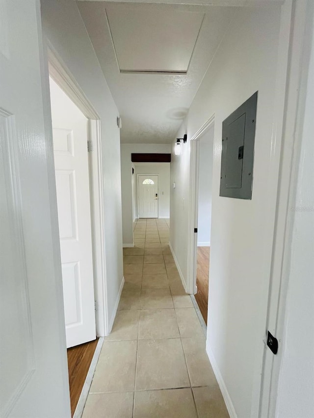 hallway featuring attic access, electric panel, baseboards, and light tile patterned flooring