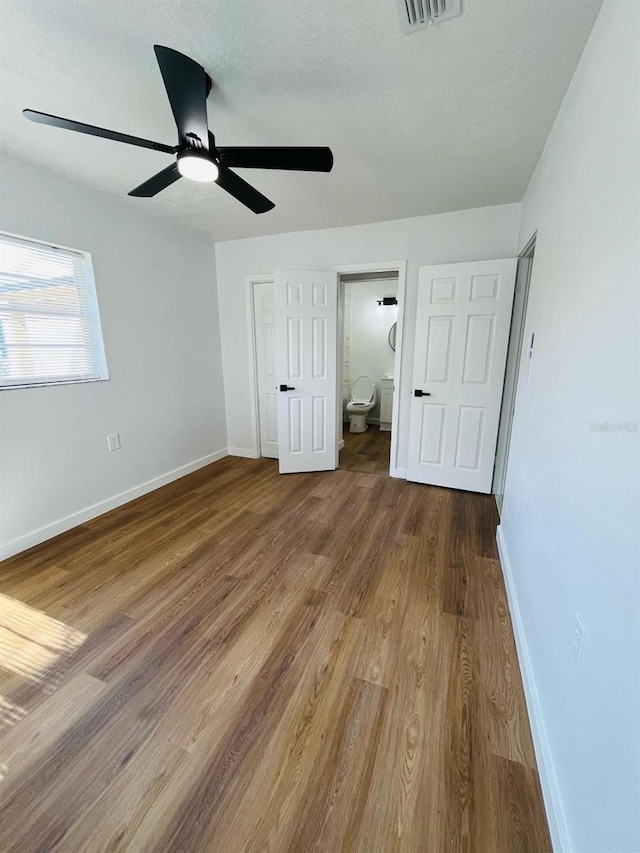 unfurnished bedroom with a textured ceiling, wood finished floors, visible vents, and baseboards