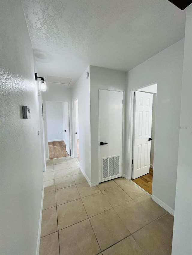 corridor with a textured ceiling, tile patterned floors, visible vents, and baseboards