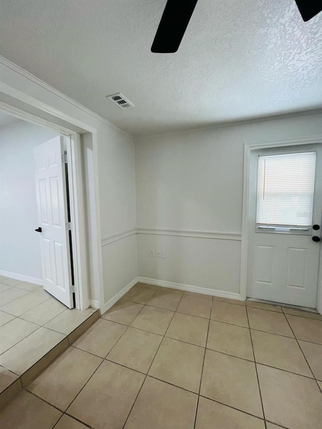 empty room with light tile patterned floors, a textured ceiling, visible vents, and a ceiling fan