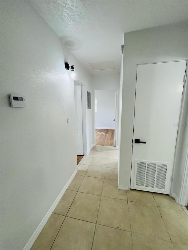 hallway featuring attic access, visible vents, baseboards, and light tile patterned flooring