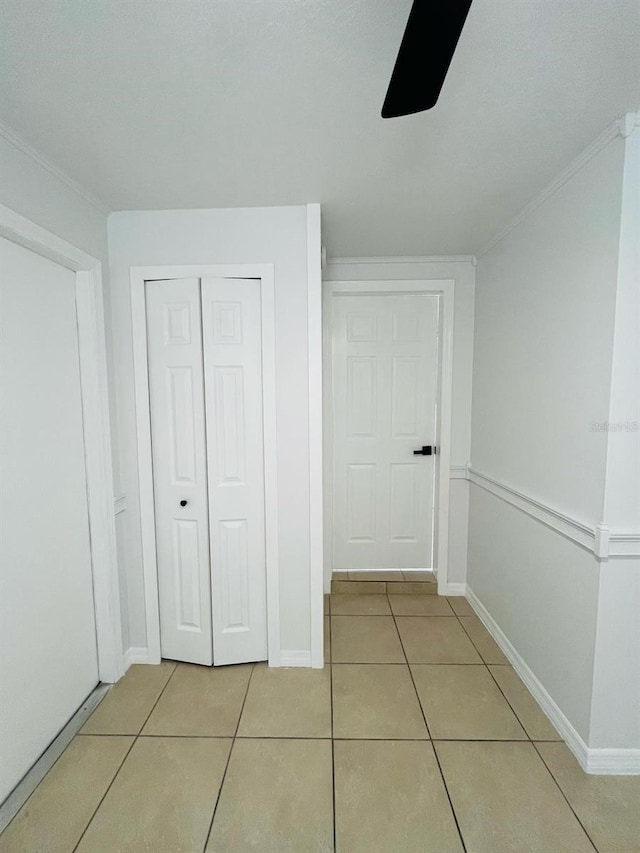 corridor with ornamental molding, light tile patterned flooring, and baseboards