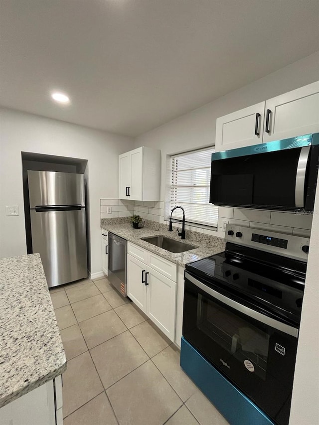 kitchen with light tile patterned flooring, stainless steel appliances, a sink, white cabinetry, and decorative backsplash