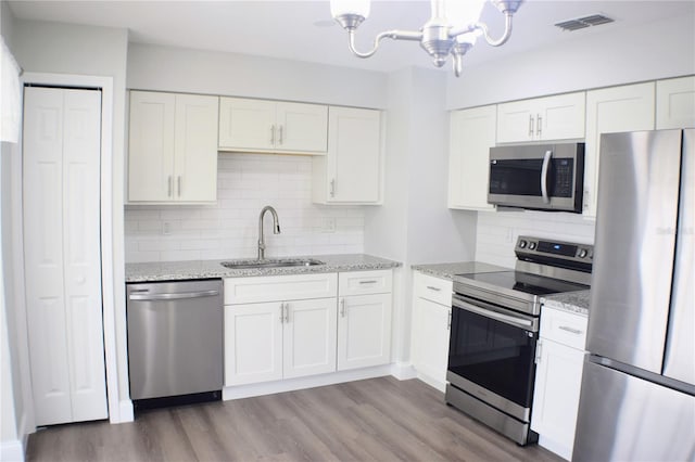 kitchen featuring stainless steel appliances, light stone counters, a sink, and white cabinetry