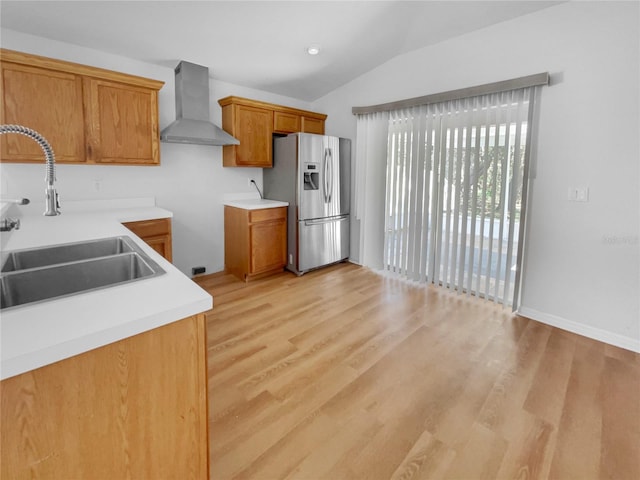 kitchen featuring brown cabinets, light countertops, a sink, wall chimney range hood, and stainless steel fridge with ice dispenser