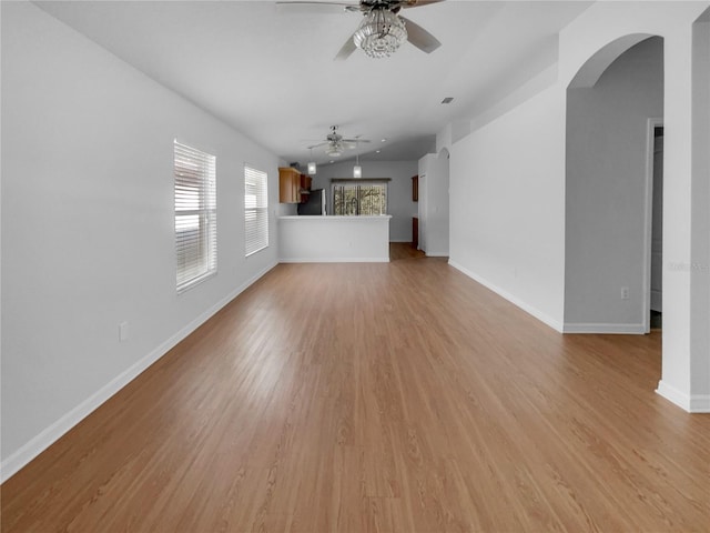 unfurnished living room with arched walkways, a ceiling fan, light wood-style flooring, and baseboards