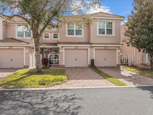 view of property featuring a garage, a tile roof, decorative driveway, and stucco siding