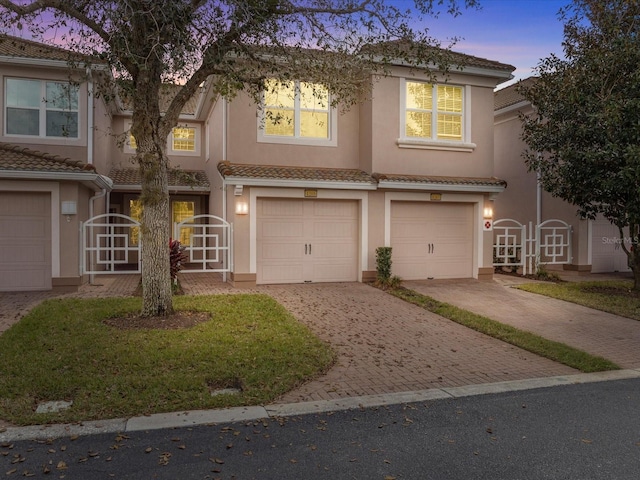 townhome / multi-family property with a garage, decorative driveway, a tiled roof, and stucco siding