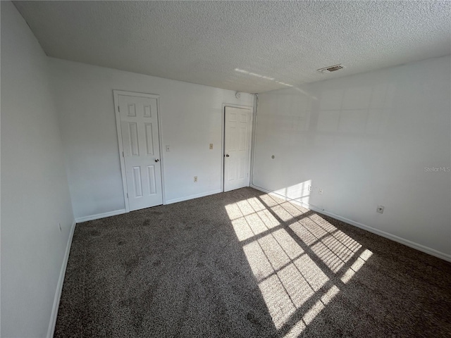 unfurnished room featuring visible vents, a textured ceiling, dark carpet, and baseboards