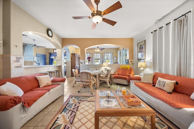 living area featuring arched walkways, a textured ceiling, light tile patterned flooring, and a ceiling fan