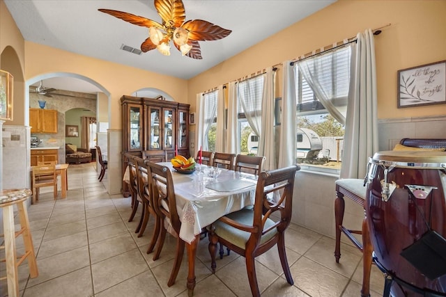 dining room featuring arched walkways, a wainscoted wall, visible vents, and a ceiling fan