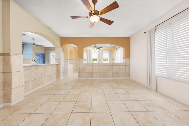 empty room with a textured ceiling, light tile patterned floors, and tile walls