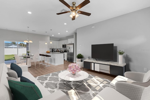 living area with ceiling fan with notable chandelier, wood finished floors, and recessed lighting