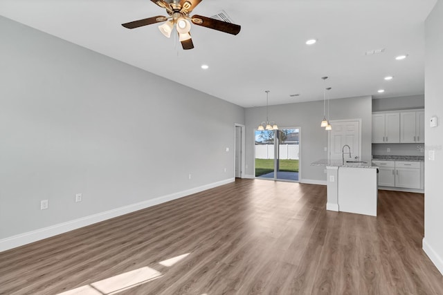 unfurnished living room with dark wood-style floors, ceiling fan with notable chandelier, baseboards, and recessed lighting