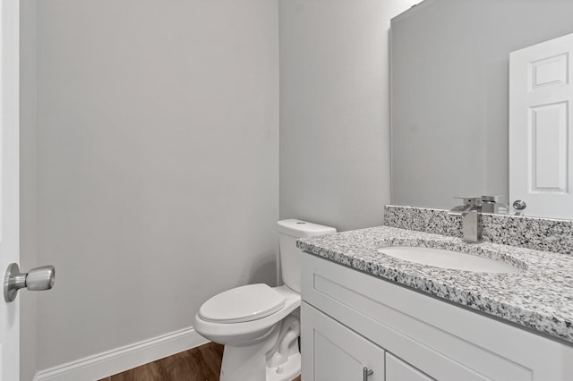 bathroom with toilet, wood finished floors, vanity, and baseboards