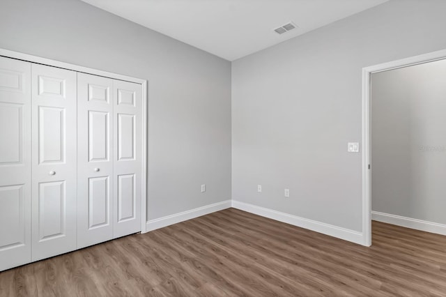 unfurnished bedroom with a closet, visible vents, baseboards, and wood finished floors