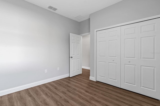 unfurnished bedroom featuring dark wood-type flooring, a closet, visible vents, and baseboards