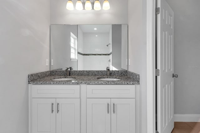 full bath featuring double vanity, tiled shower, a sink, and tile patterned floors