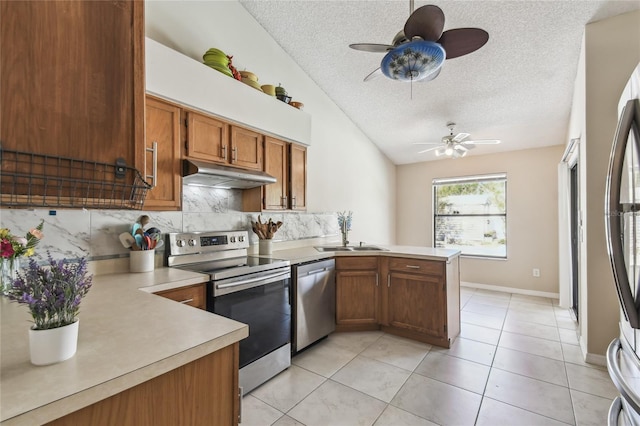 kitchen featuring under cabinet range hood, a sink, stainless steel appliances, a peninsula, and light countertops