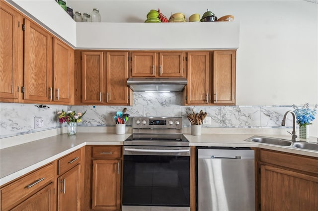 kitchen with brown cabinetry, a sink, stainless steel appliances, light countertops, and under cabinet range hood