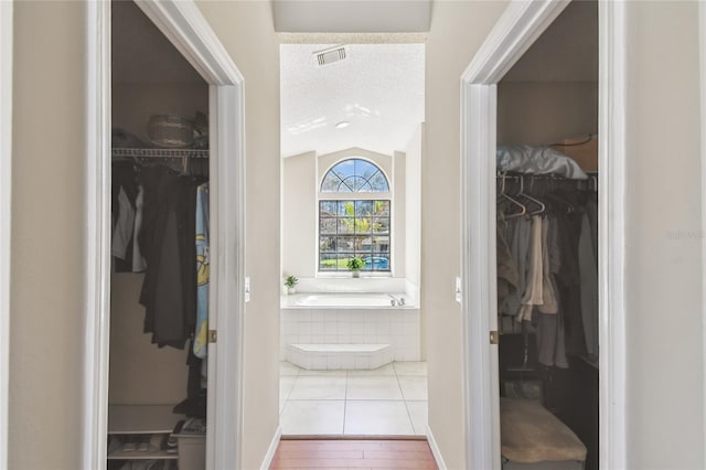 corridor with visible vents, a textured ceiling, wood finished floors, and vaulted ceiling