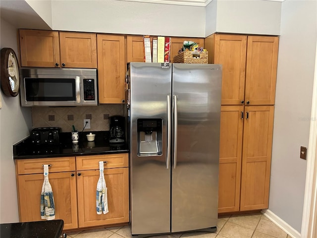 kitchen with dark countertops, light tile patterned floors, decorative backsplash, brown cabinets, and appliances with stainless steel finishes