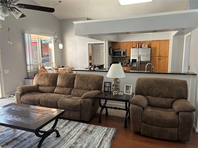 living room with ceiling fan with notable chandelier, a textured ceiling, dark wood finished floors, and vaulted ceiling